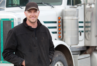 Image of a truck driver wearing a black jacket and hat standing in front of a white and green truck.