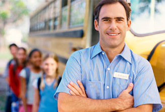 Image of male bus driving wearing blue shirt standing in front of a blurred out school bus and a line of 4 children