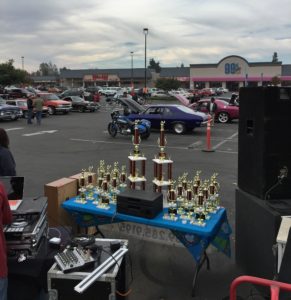 Image of tophies arranged on a table in front of the DJ booth at Toys for Tots car show event