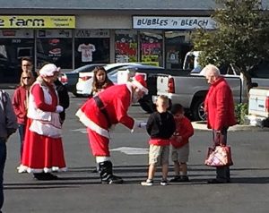 Image of a crowd of people in the parking lot at Toys for Tots event with Santa and Mrs. Claus leaning over talking with small children