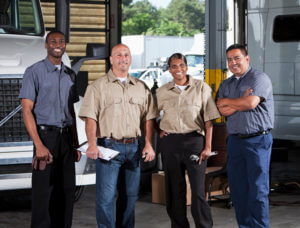 Image of four maintenance workers standing in front of trucks in repair shop
