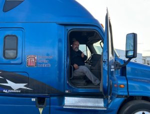 Trucker giving a thumbs up and smiling while sitting in a blue ACI semi truck
