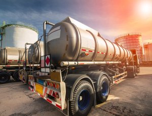 Stainless steel tanker trucks parked at a fuel storage facility with large tanks