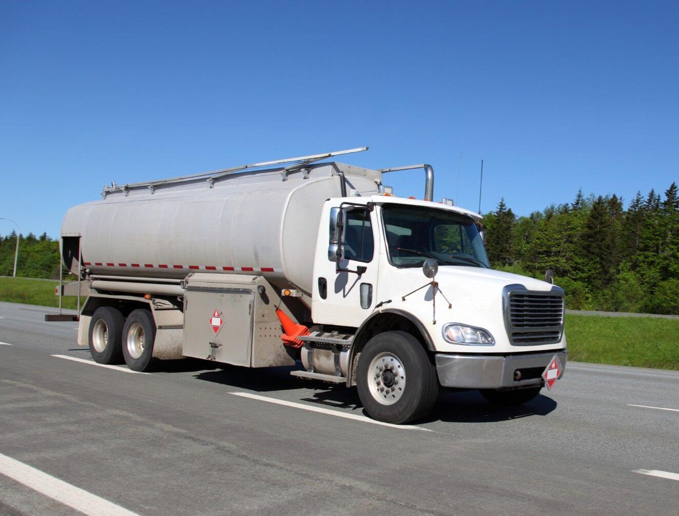 A white tanker truck carrying liquid cargo driving on a highway 