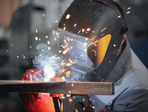 welder with helmet down welding on metal bar