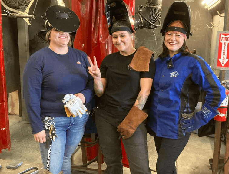 Three female welding students smiling, welding masks on their heads
